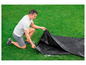 Muž skládá černou plachtu na trávě.