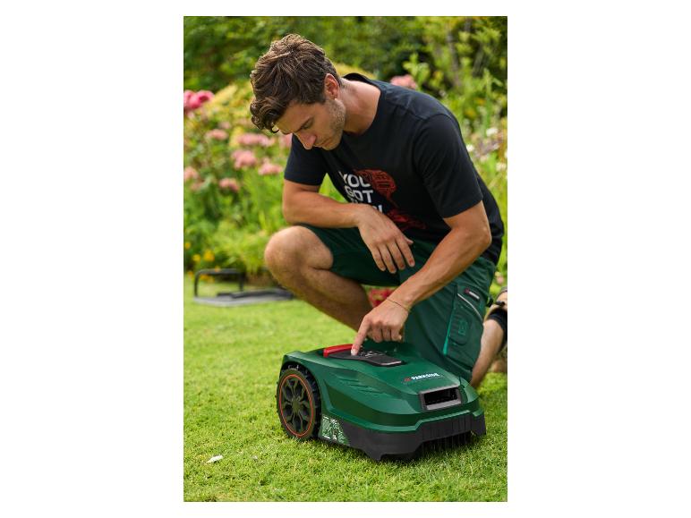 Muž klečící na trávníku, nastavující robotickou sekačku.