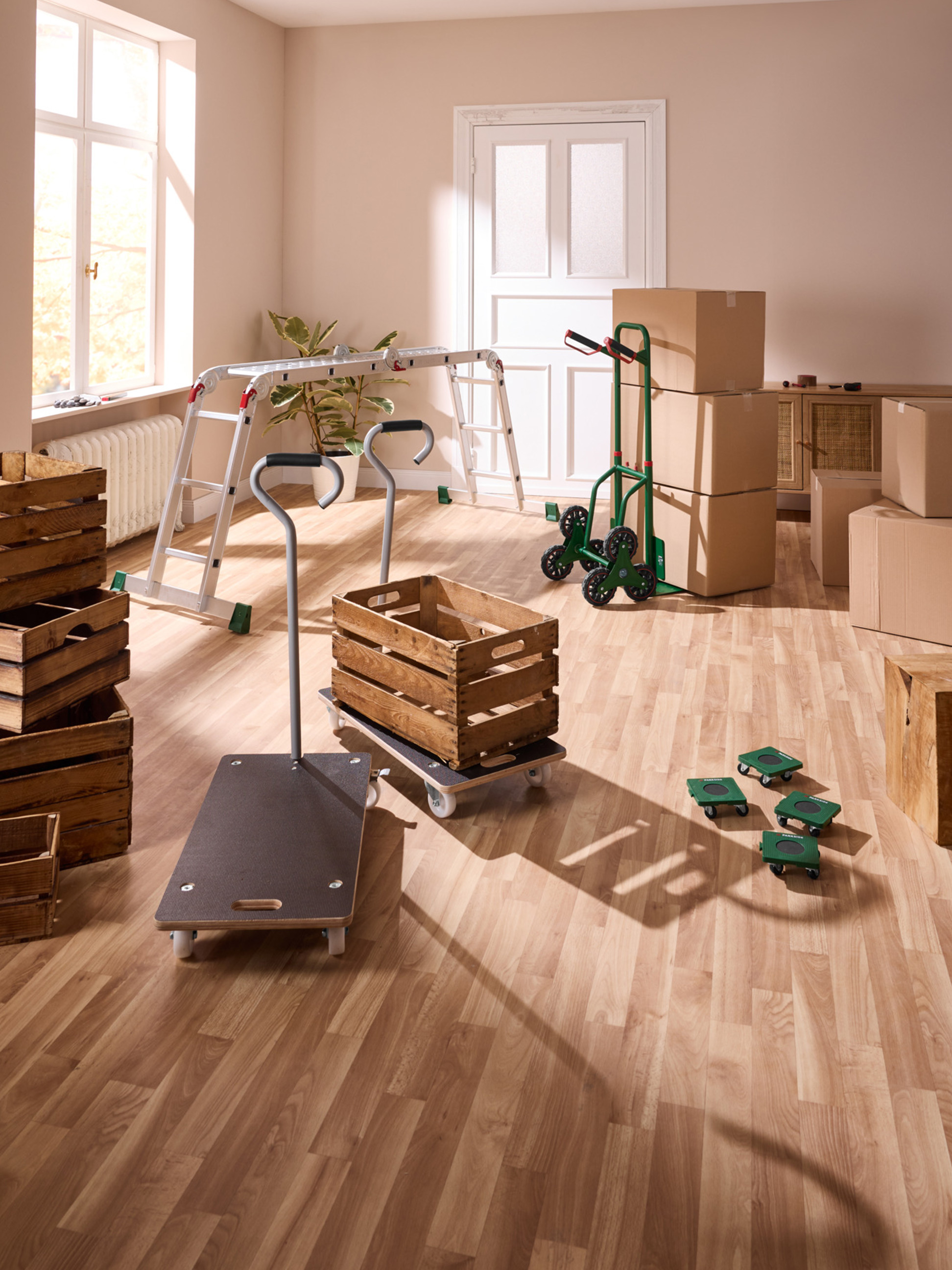 Přepravní vozíky a dřevěné bedny v pokoji s parketami, připravené k stěhování.