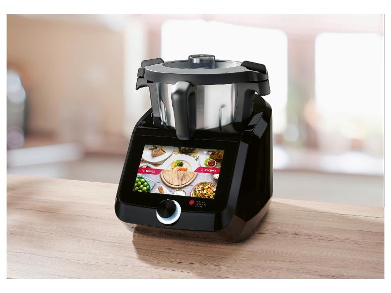 Černý kuchyňský robot s dotykovou obrazovkou zobrazující režimy a recepty, na dřevěné desce.