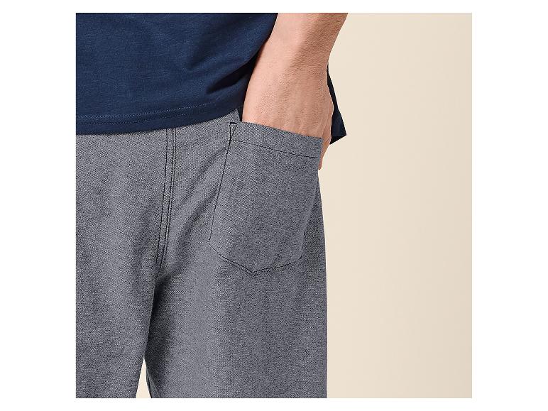 Muž v modrém tričku a šedých šortkách s rukou v kapse.