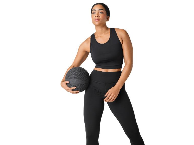 Žena v černém sportovním oblečení drží medicinbal.