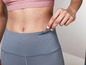 Žena v šedých legínách a růžové sportovní podprsence s klíčem v kapse.