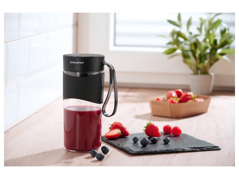 Přenosný mixér SilverCrest s červeným smoothie a čerstvým ovocem na dřevěné desce.