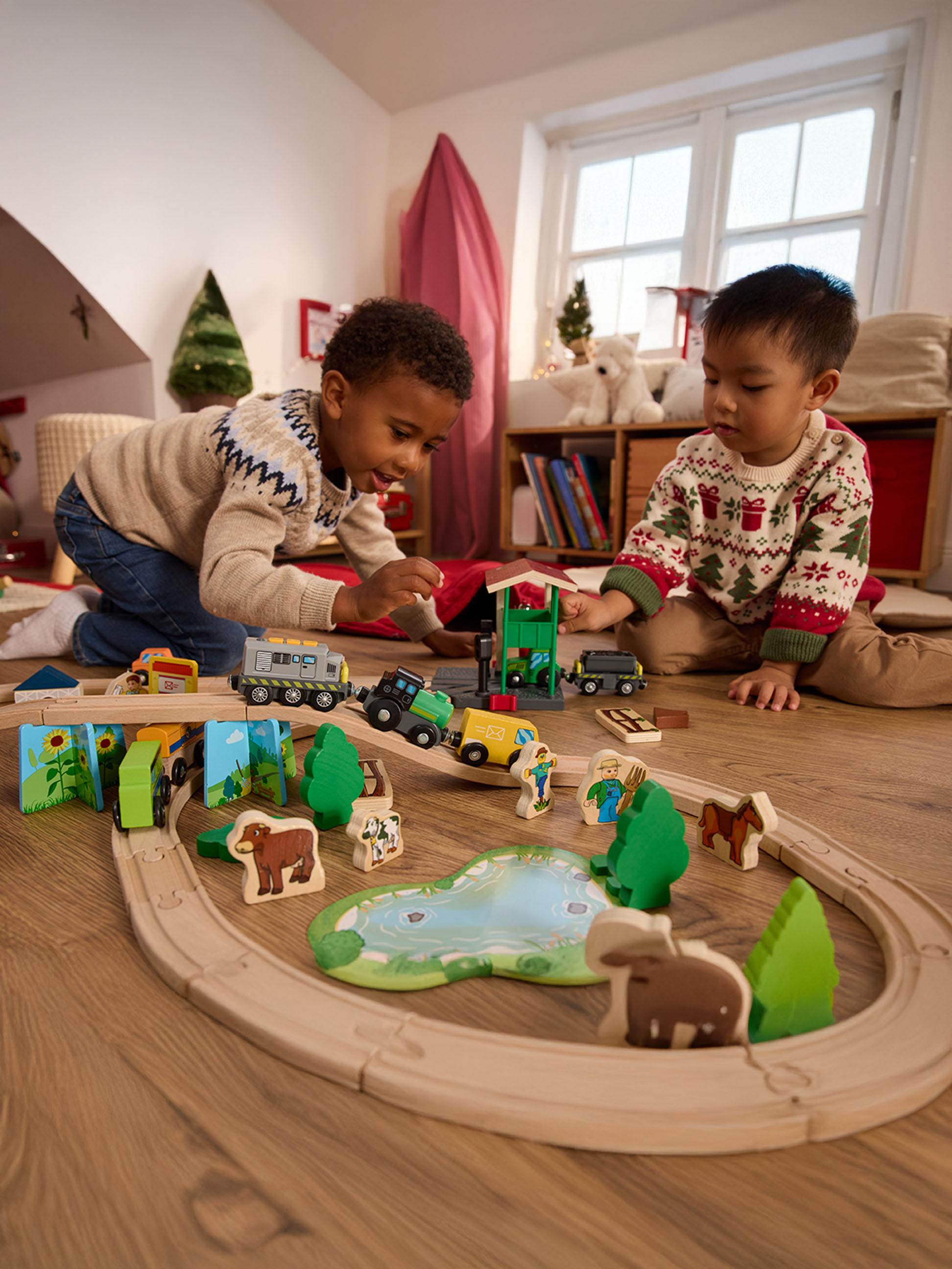 Dva chlapci si hrají s dřevěným vláčkem a figurkami zvířat na dřevěné podlaze.