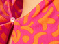 Detailní záběr na růžový a oranžový kvetinový oděv s knoflíkem.