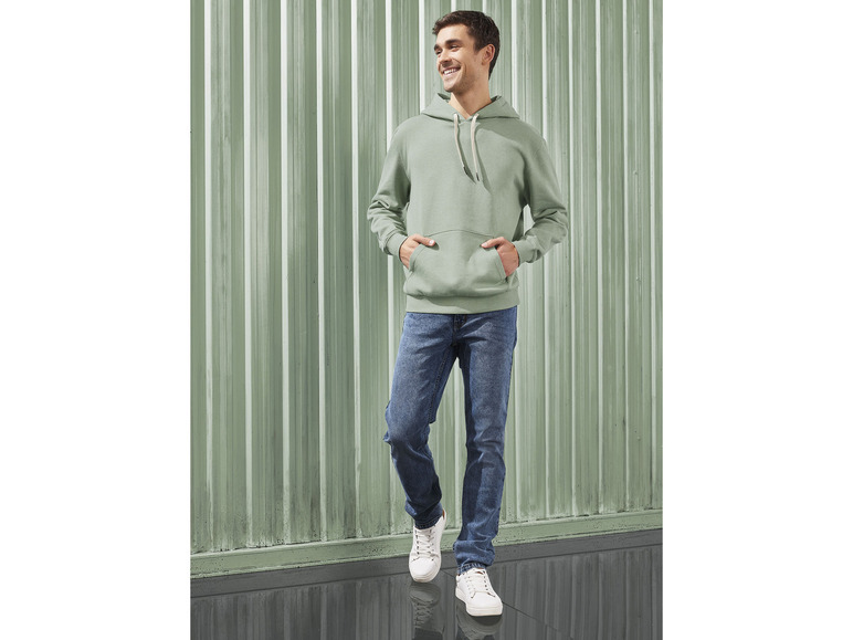 Muž v zelené mikině a modrých džínách.
