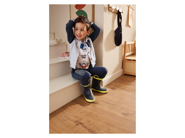 Malý chlapec sedí na schodech v oblečení a holínkách Paw Patrol.