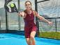 Žena v bordó sportovních šatech hraje padel s černou raketou a žlutým míčkem.