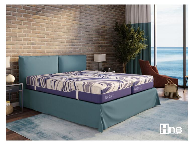 Ložnice s postelí Hn8 Sequal, cihlovou zdí a výhledem na moře.