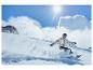 Snowboarder sjíždí s kopce v slunečný den.