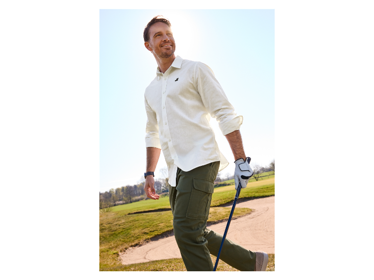 Muž hrající golf v bílé košili a cargo kalhotách.
