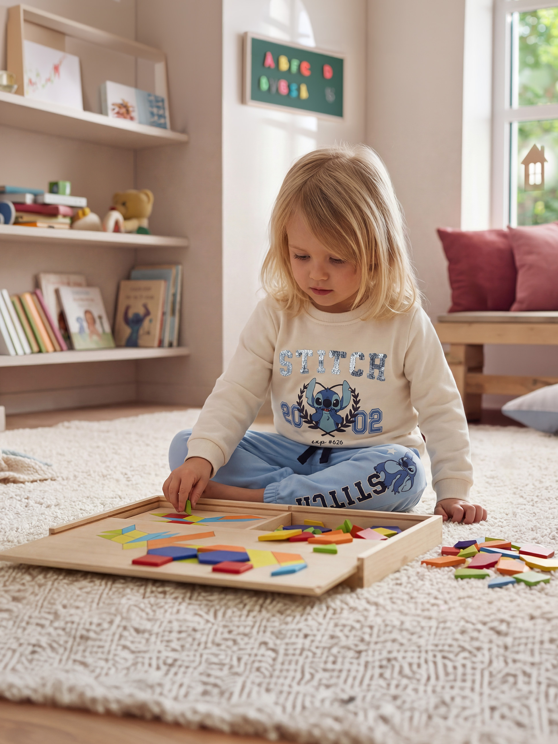 Dítě si hraje s barevným dřevěným puzzle na huňatém koberci, oblečené v mikině a teplácích.