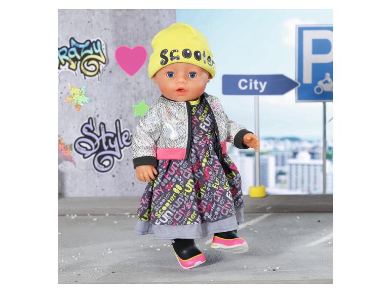 Panenka v šatech s městským potiskem, stříbrné bundě a žluté čepici s nápisem „Scooter”.