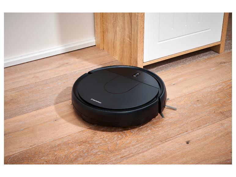 Robotický vysavač SilverCrest na dřevěné podlaze vedle bílé skříně