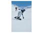 Snowboardista v vzorovaných kalhotách a světle modré bundě sjíždí zasněžený svah.