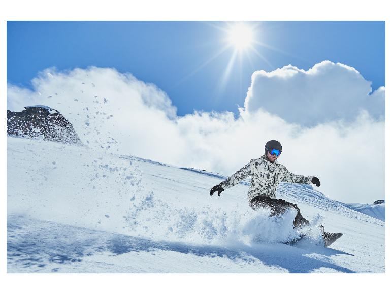 Snowboarder sjíždí s kopce v slunečný den.
