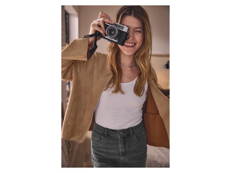 Žena v béžové bundě a džínové sukni fotí starým fotoaparátem.