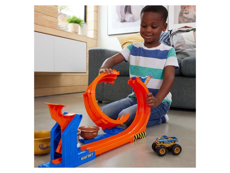 Usmívající se chlapec si hraje se sadou dráhy Hot Wheels Monster Trucks a autem.