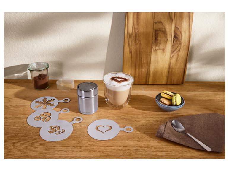 Kávové šablony a kakaový posypovač s latte a makronkami na dřevěném stole.