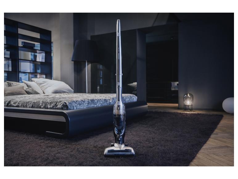 Tyčový vysavač Grundig v moderní ložnici s postelí a kobercem.