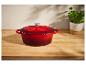 Červený litinový hrnec s pokličkou na dřevěném stole.