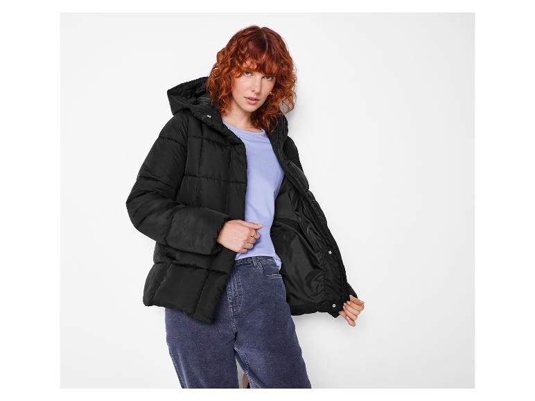 Zrzavá žena v černé prošívané bundě a džínách.