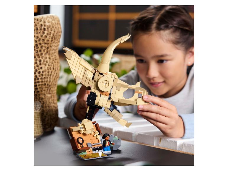 Dívka skládá LEGO kostru dinosaura, s LEGO minifigurkou vedle ní.