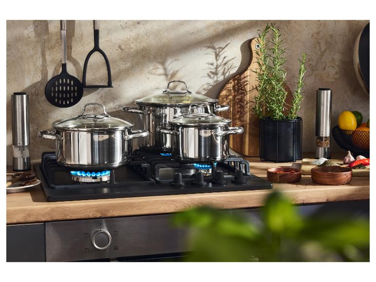 Tři nerezové hrnce na plynovém sporáku s kuchyňským náčiním a bylinkami