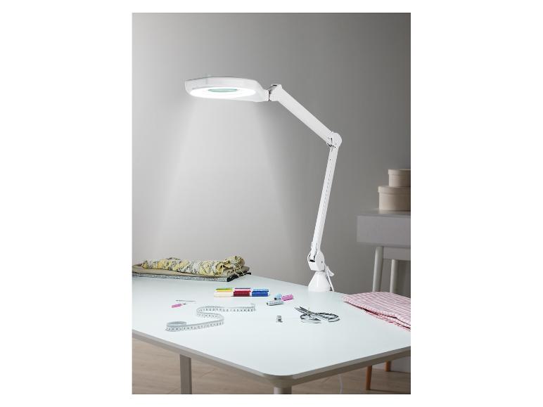 Bílá stolní lampa s lupou a šicími potřebami na bílém stole.