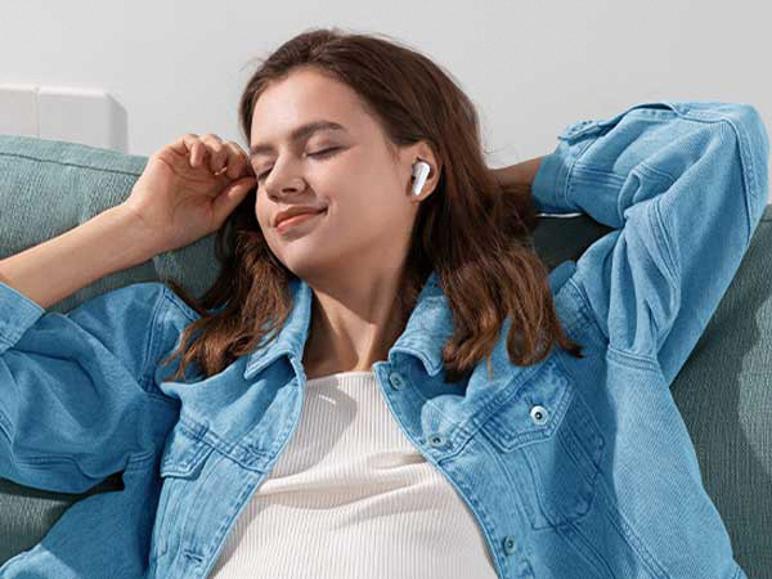 Žena relaxuje na pohovce a poslouchá hudbu s bílými sluchátky do uší.