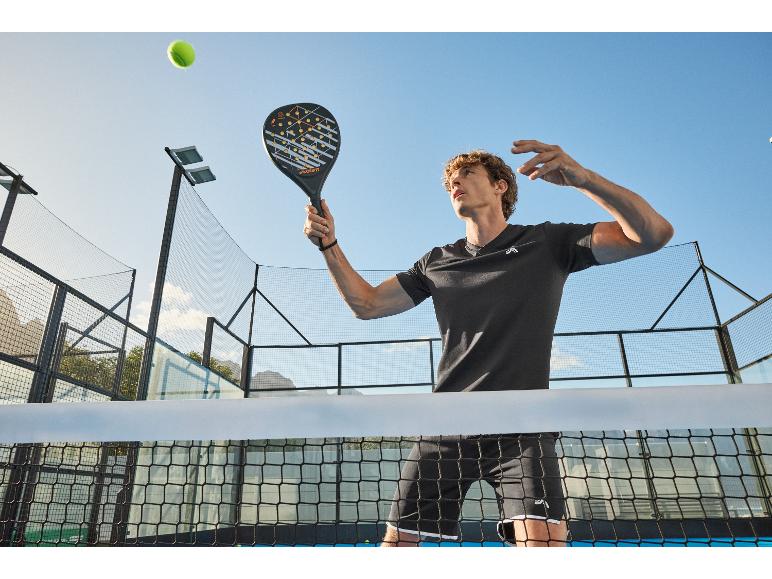 Muž hrající padel, držící padelovou raketu, s tenisovým míčkem ve vzduchu.