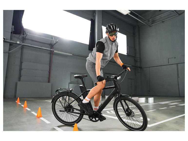 Muž v reflexní vestě a cyklistických brýlích na kole, trénující jízdu mezi kužely.