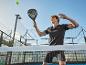 Muž hrající padel s raketou, míčkem a kurtem v pozadí.