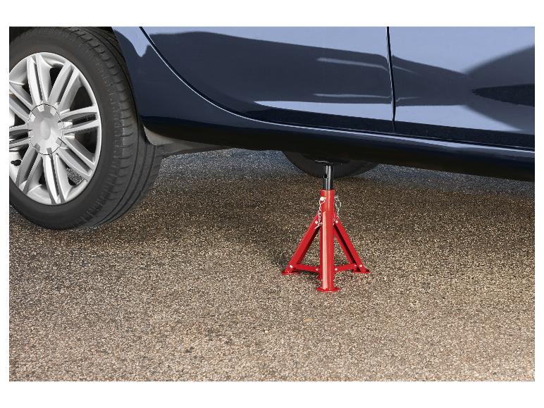 Auto podepřené červeným stojanem na zvedák na asfaltovém povrchu.