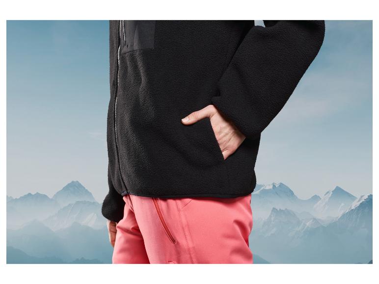 Černá fleecová bunda a růžové kalhoty před pozadím hor