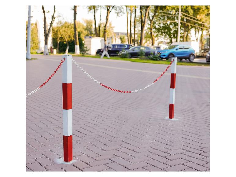 Červeno-bílé zábranné sloupky s řetězem na ulici s zaparkovanými auty.