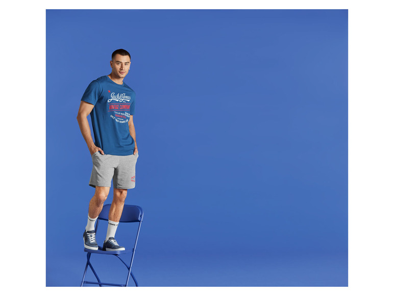Muž v tričku a šortkách Jack & Jones na modrém pozadí.