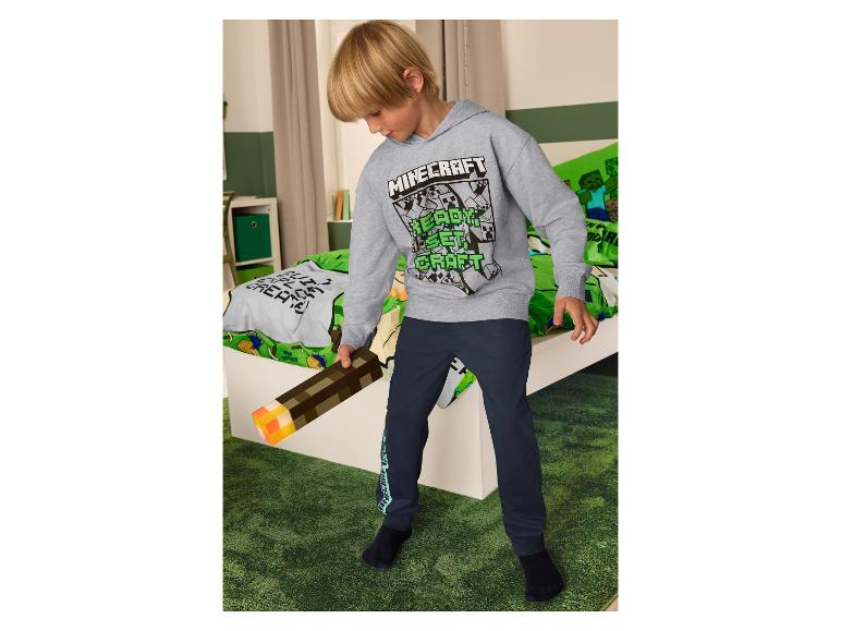 Chlapec v mikině Minecraft a tmavě modrých kalhotách, držící pochodeň Minecraft.