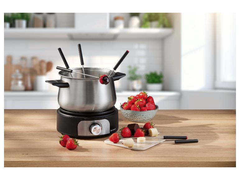 Elektrická fondue souprava s jahodami, čokoládou a banány na dřevěném stole.