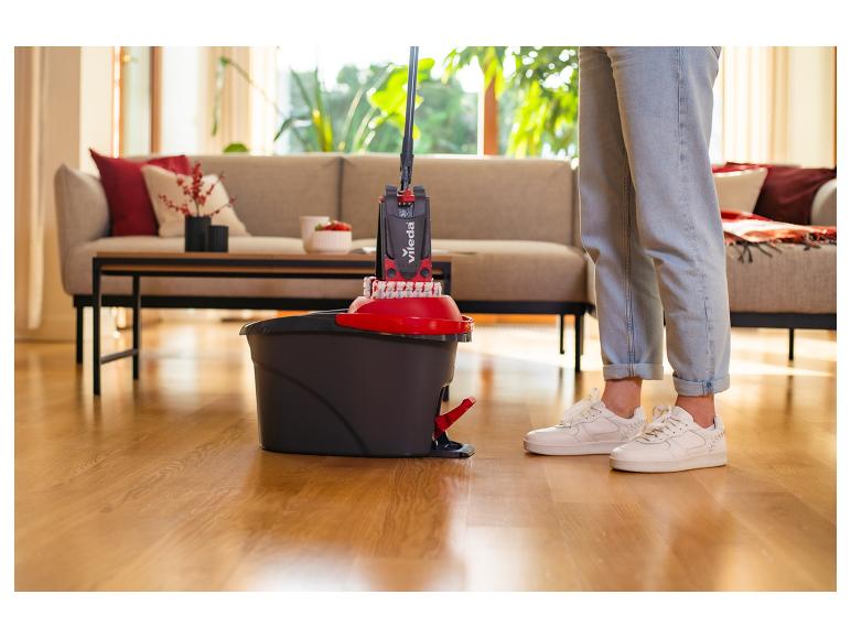 Osoba používající mop a kbelík Vileda k čištění dřevěné podlahy v obývacím pokoji.