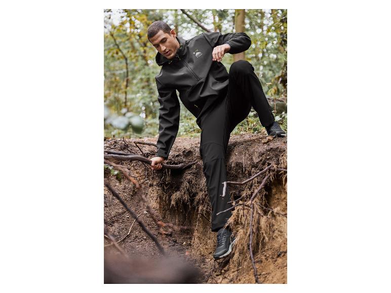 Muž v černé bundě a kalhotách Mountain Warehouse v lese.