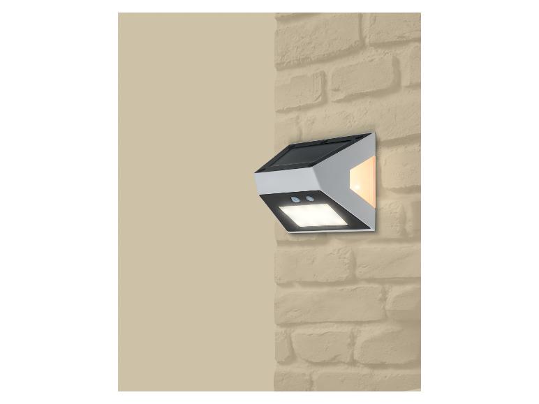 Solární nástěnná lampa s pohybovým senzorem a dvěma světly, připevněná na cihlové zdi.
