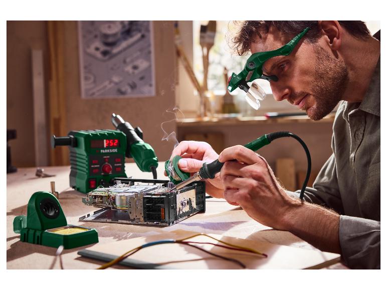 Muž pájí elektroniku s vybavením Parkside, včetně pájecí stanice a zvětšovacích brýlí.