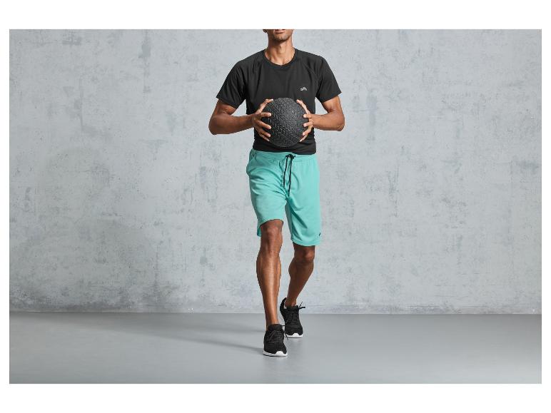 Muž v černém tričku a modrých šortkách drží medicinbal.