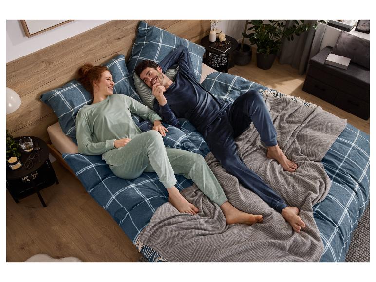 Usmívající se pár relaxuje v posteli, oblečený v ladících pyžamech, s kostkovaným povlečením.