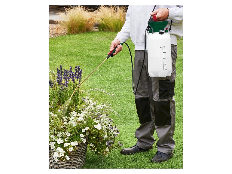 Osoba stříkající rostliny na zahradě ramenním tlakovým postřikovačem.
