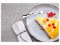 Kousek cheesecaku s mangovou polevou a červeným rybízem na talíři s vidličkou.