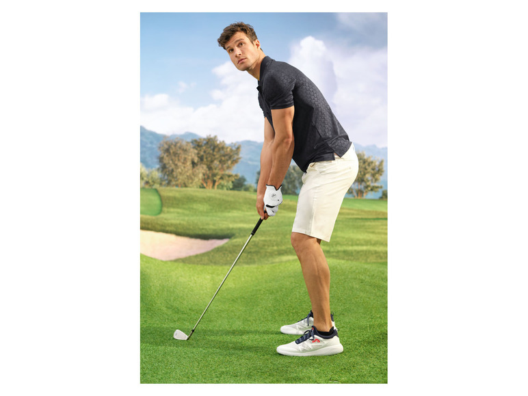 Muž v golfovém oblečení, včetně trička s krátkým rukávem a šortů, na golfovém hřišti.