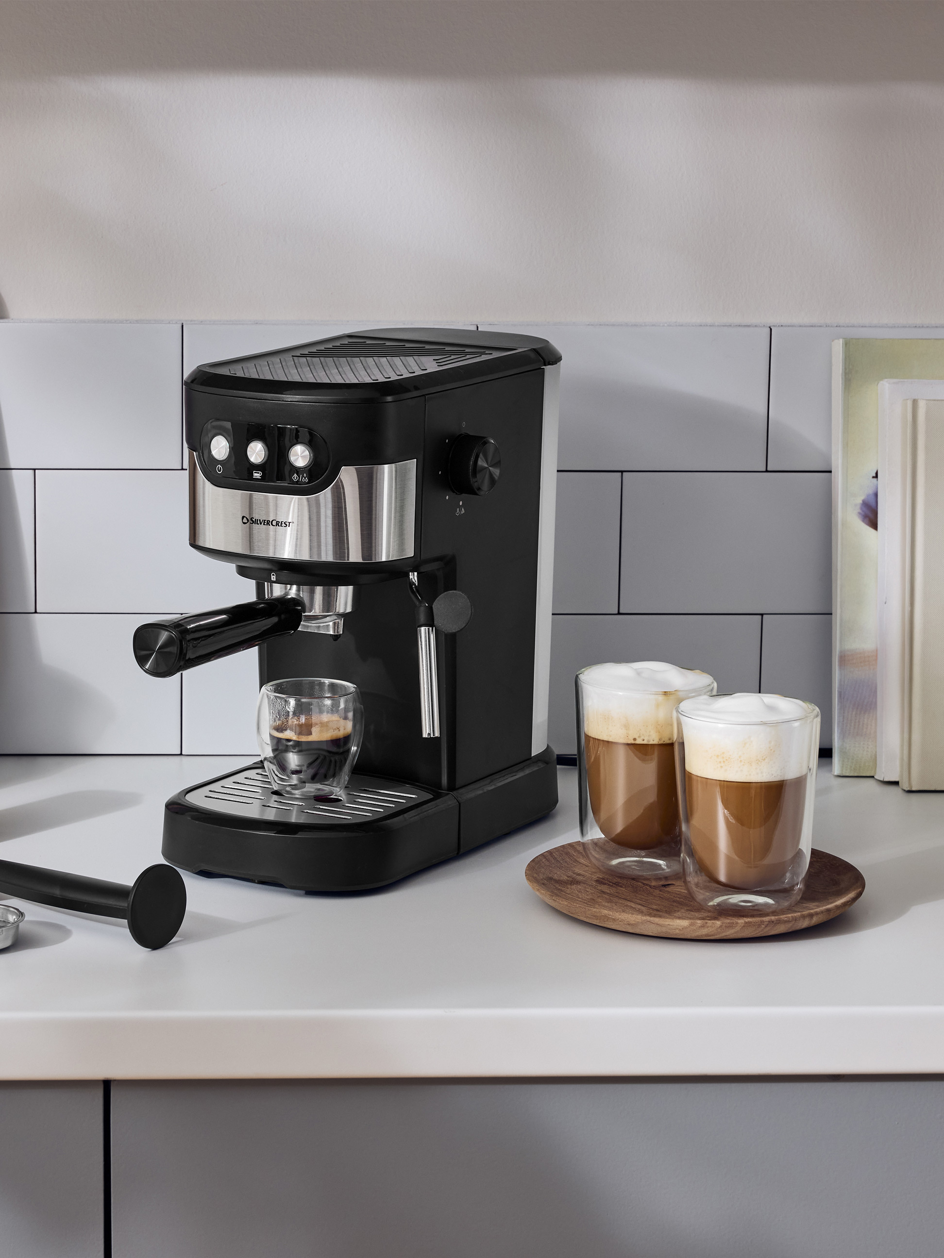 Černý kávovar na espresso na bílé kuchyňské lince se dvěma šálky kávy.